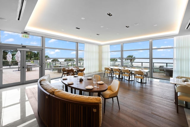 dining space featuring a raised ceiling, a water view, a wealth of natural light, and expansive windows