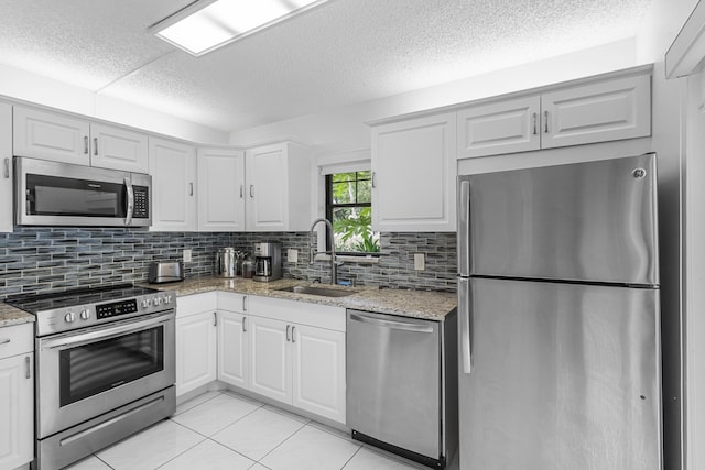 kitchen with light stone countertops, appliances with stainless steel finishes, sink, light tile patterned floors, and white cabinetry