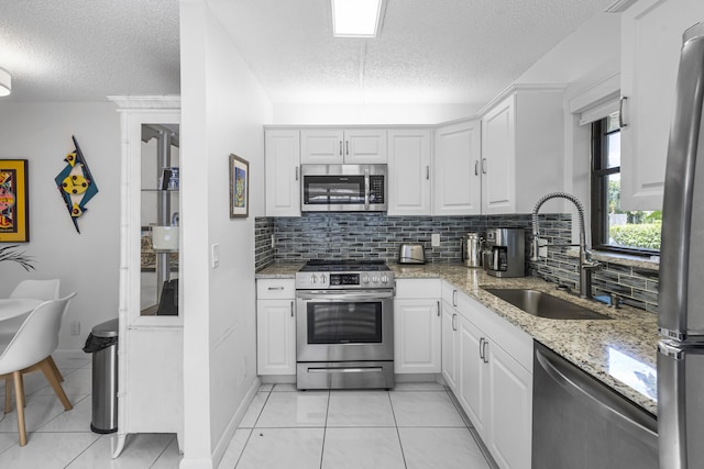 kitchen with light stone countertops, sink, stainless steel appliances, a textured ceiling, and white cabinets