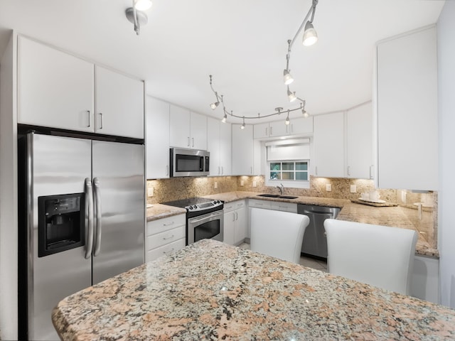 kitchen with kitchen peninsula, appliances with stainless steel finishes, tasteful backsplash, sink, and white cabinetry