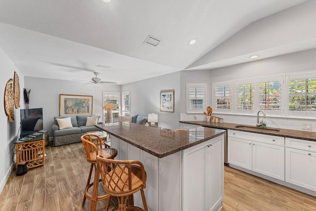 kitchen featuring a breakfast bar, sink, light hardwood / wood-style flooring, white cabinets, and lofted ceiling