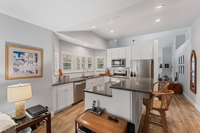 kitchen with white cabinetry, a center island, stainless steel appliances, dark stone countertops, and vaulted ceiling