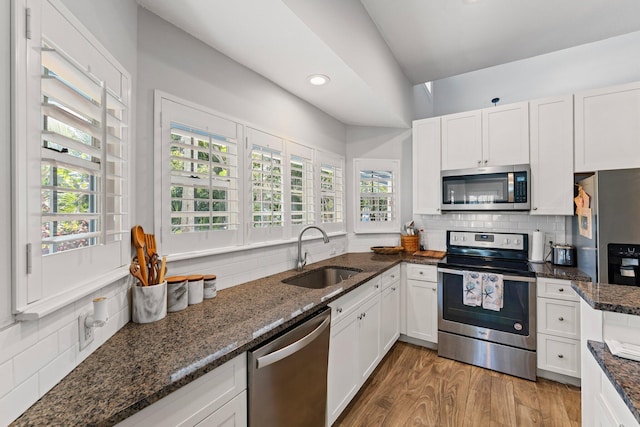 kitchen with appliances with stainless steel finishes, white cabinetry, dark stone countertops, and sink