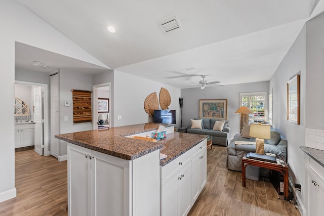 kitchen with white cabinets, light hardwood / wood-style floors, vaulted ceiling, and dark stone countertops