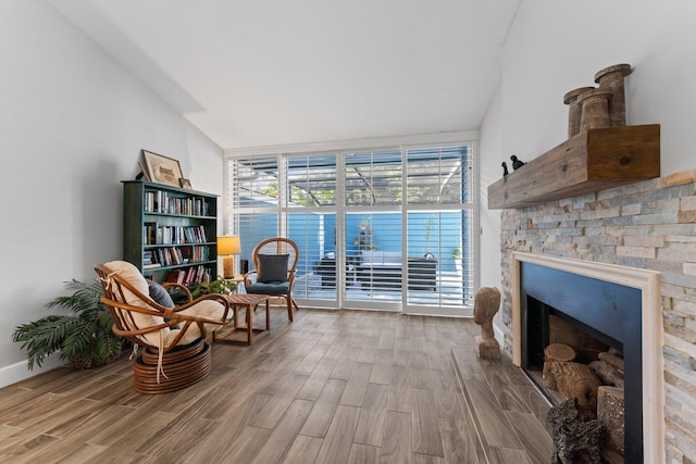 living area featuring wood-type flooring, a stone fireplace, and expansive windows