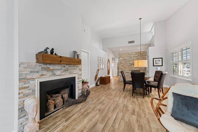 living room with a stone fireplace, light hardwood / wood-style flooring, and a towering ceiling