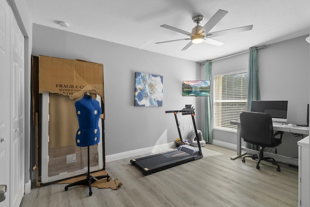 workout room with ceiling fan, light wood-type flooring, and a textured ceiling