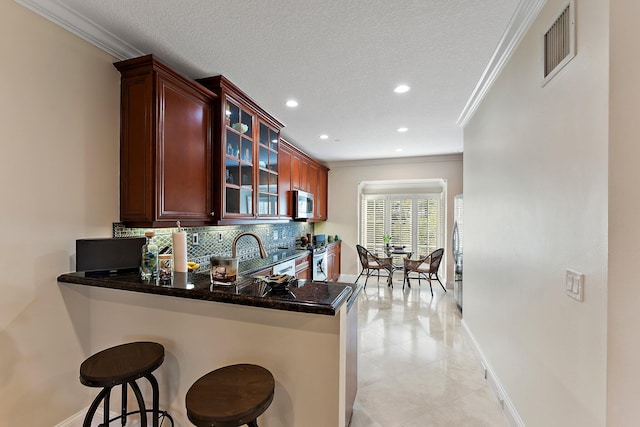 kitchen with backsplash, crown molding, a textured ceiling, a kitchen bar, and kitchen peninsula