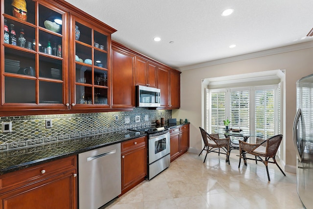 kitchen featuring dark stone counters, ornamental molding, tasteful backsplash, light tile patterned flooring, and stainless steel appliances