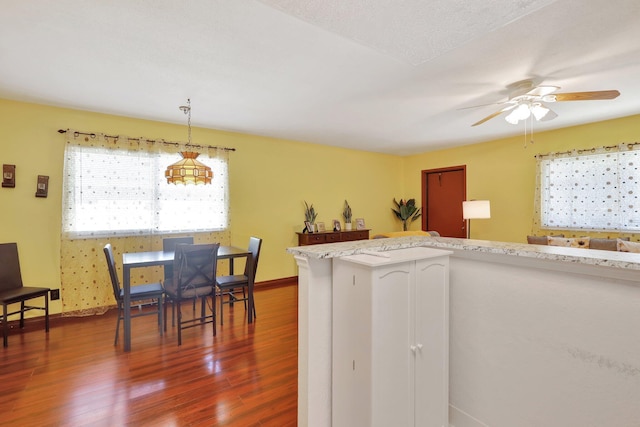 kitchen with ceiling fan, light stone countertops, hanging light fixtures, and dark wood-type flooring