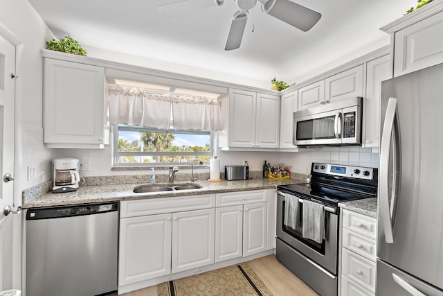 kitchen with decorative backsplash, light stone countertops, stainless steel appliances, sink, and white cabinetry