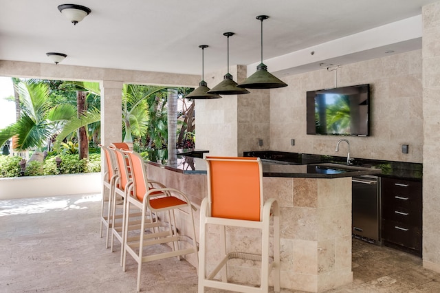 bar featuring pendant lighting, sink, stainless steel dishwasher, and tile walls