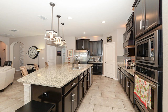 kitchen with sink, hanging light fixtures, stainless steel appliances, a kitchen island with sink, and light tile patterned floors