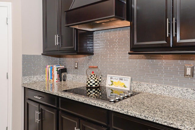 kitchen featuring premium range hood, light stone counters, tasteful backsplash, dark brown cabinetry, and stovetop