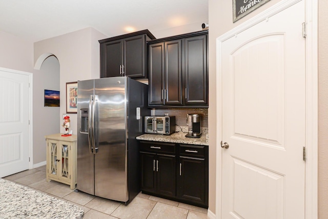 kitchen with tasteful backsplash, stainless steel fridge, light tile patterned floors, and light stone countertops