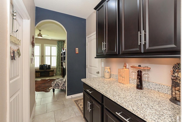 kitchen with dark brown cabinetry, ceiling fan, light tile patterned floors, and light stone countertops