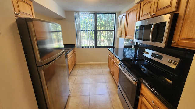 kitchen with light tile patterned flooring, dark stone countertops, and appliances with stainless steel finishes