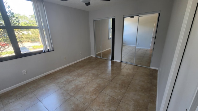 unfurnished bedroom with light tile patterned floors, two closets, and ceiling fan