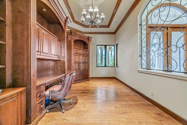 unfurnished office featuring a raised ceiling, built in desk, ornamental molding, light hardwood / wood-style floors, and a chandelier