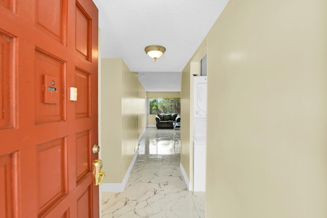 hall with stacked washing maching and dryer and a textured ceiling