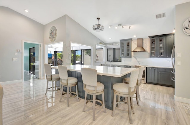 kitchen with a center island, sink, wall chimney range hood, high vaulted ceiling, and decorative light fixtures