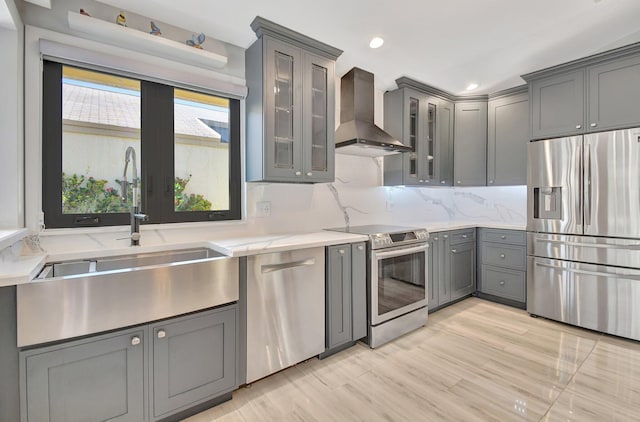 kitchen with wall chimney range hood, sink, gray cabinets, light wood-type flooring, and appliances with stainless steel finishes