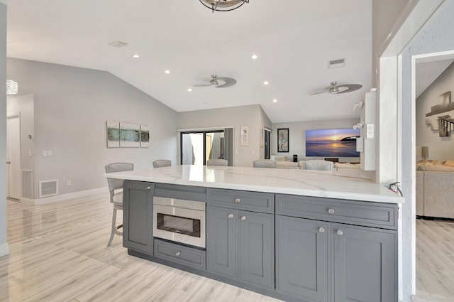 kitchen featuring a breakfast bar area, gray cabinets, ceiling fan, and light stone counters