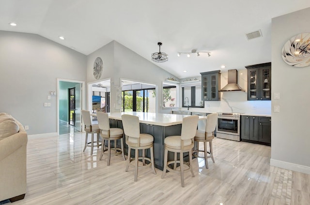 kitchen featuring wall chimney exhaust hood, stainless steel range with electric cooktop, decorative light fixtures, a center island, and lofted ceiling