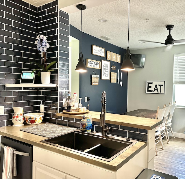 kitchen with dishwasher, white cabinets, sink, light wood-type flooring, and decorative light fixtures