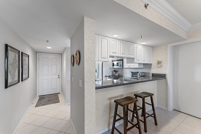 kitchen with kitchen peninsula, light tile patterned floors, white cabinetry, and dark stone counters