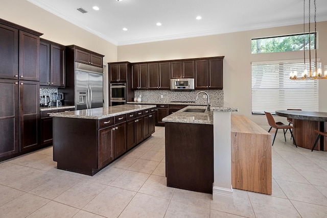 kitchen featuring appliances with stainless steel finishes, a center island with sink, hanging light fixtures, and crown molding