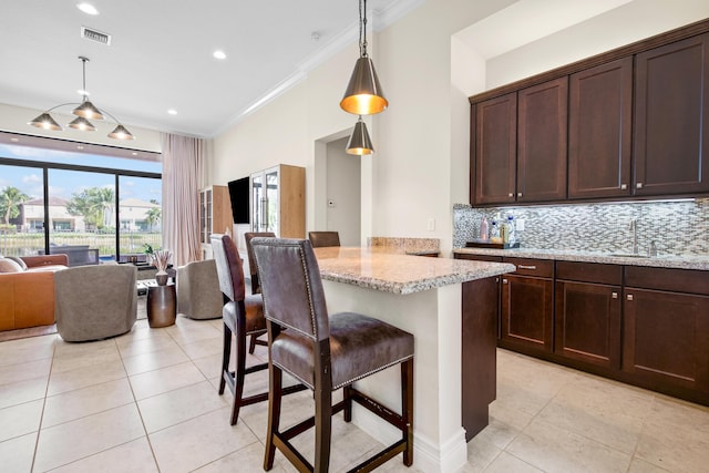 kitchen featuring light stone countertops, a kitchen bar, backsplash, ornamental molding, and pendant lighting