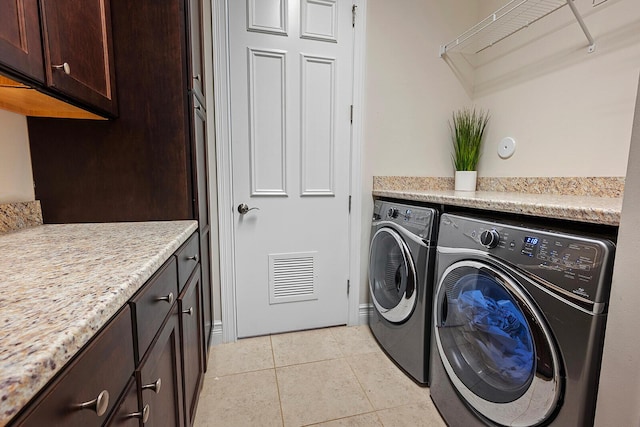 clothes washing area featuring washer and clothes dryer, light tile patterned flooring, and cabinets