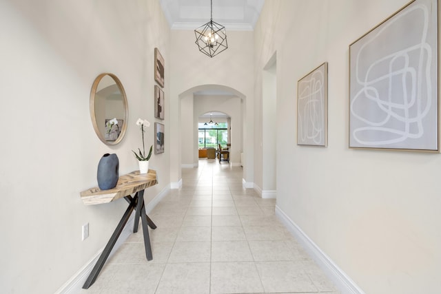 corridor with light tile patterned flooring, ornamental molding, a high ceiling, and a chandelier