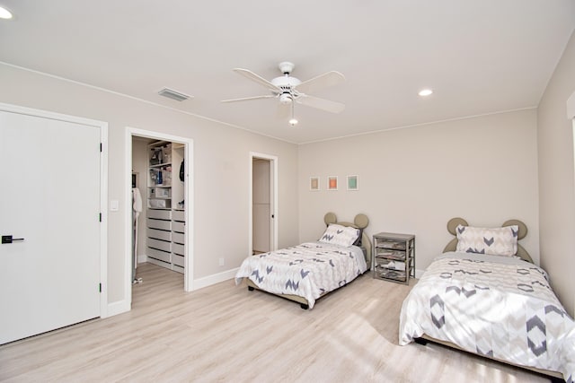 bedroom with a walk in closet, ceiling fan, a closet, and light wood-type flooring