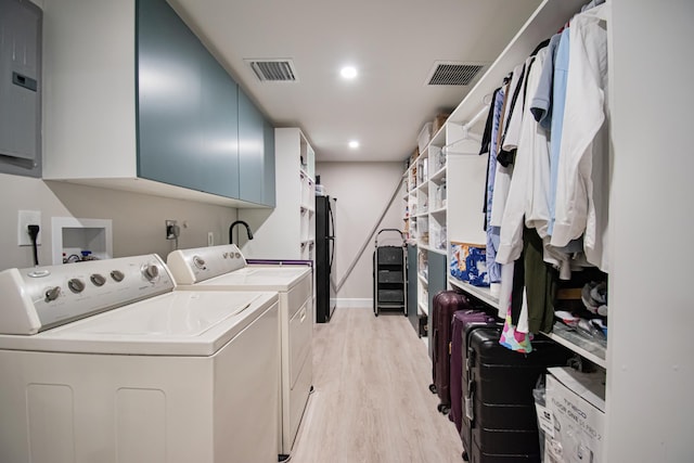 laundry area with washing machine and clothes dryer, electric panel, light hardwood / wood-style flooring, and cabinets