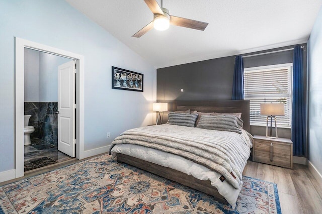 bedroom featuring ceiling fan, ensuite bathroom, light hardwood / wood-style floors, and vaulted ceiling