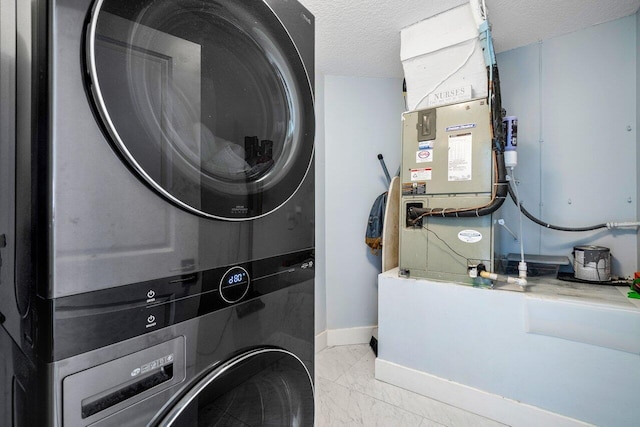 laundry area with heating unit, stacked washing maching and dryer, and a textured ceiling