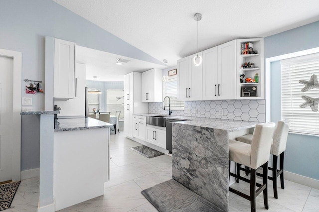 kitchen with kitchen peninsula, white cabinetry, light stone countertops, and vaulted ceiling