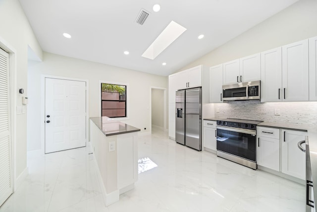 kitchen featuring vaulted ceiling with skylight, decorative backsplash, white cabinetry, and appliances with stainless steel finishes