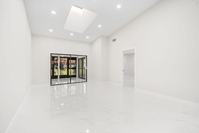 spare room with a towering ceiling and a skylight