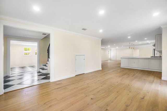 unfurnished living room featuring crown molding, sink, and light hardwood / wood-style floors