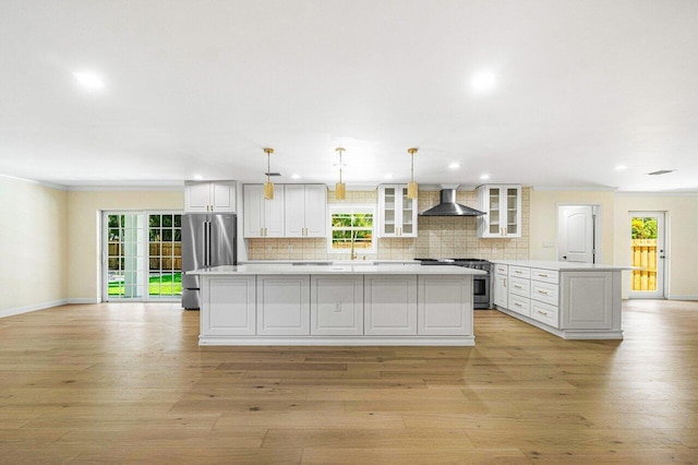 kitchen with wall chimney exhaust hood, light hardwood / wood-style floors, decorative light fixtures, a kitchen island, and stainless steel appliances