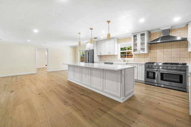 kitchen featuring a center island, wall chimney range hood, light hardwood / wood-style floors, white cabinetry, and stainless steel appliances