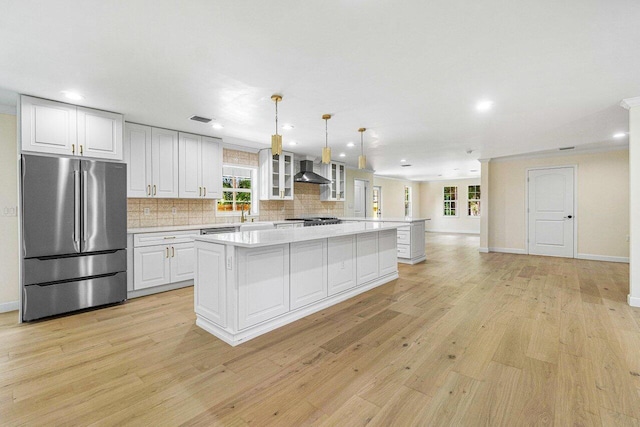 kitchen with a center island, wall chimney range hood, light hardwood / wood-style flooring, stainless steel fridge, and white cabinets