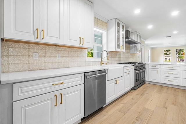 kitchen featuring white cabinets, light hardwood / wood-style floors, wall chimney range hood, and appliances with stainless steel finishes