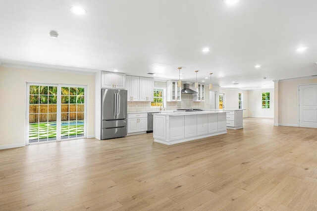 kitchen with white cabinets, hanging light fixtures, wall chimney exhaust hood, a kitchen island, and stainless steel appliances