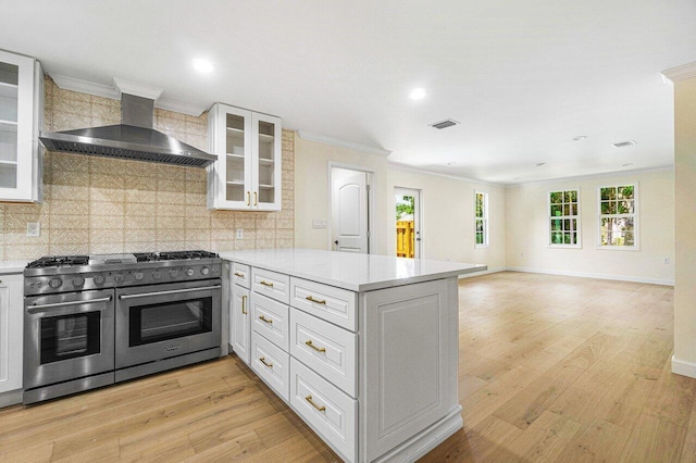 kitchen featuring kitchen peninsula, wall chimney range hood, light hardwood / wood-style flooring, range with two ovens, and white cabinets