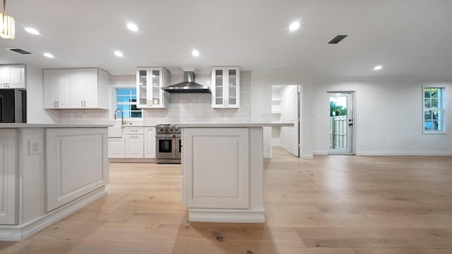 kitchen with wall chimney exhaust hood, white cabinetry, stainless steel appliances, and light hardwood / wood-style flooring