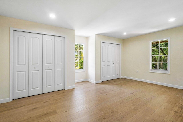 unfurnished bedroom featuring multiple closets, light hardwood / wood-style flooring, and multiple windows